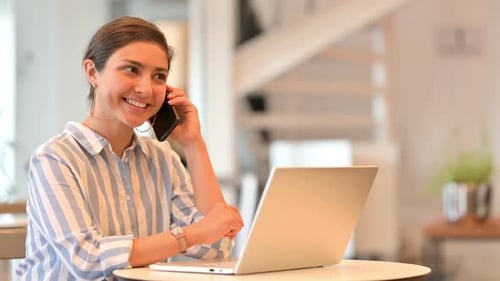 Young Woman Uses Laptop and Talks on Phone