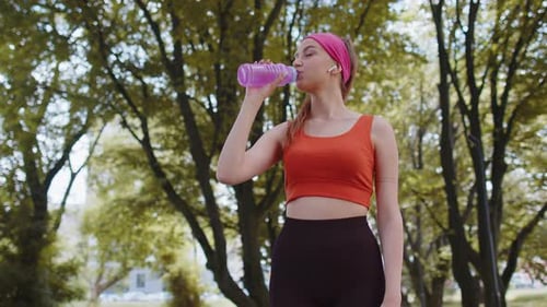 Athletic Fit Sport Runner Adult Girl Drinking Water From Bottle After Training Exercising in Park