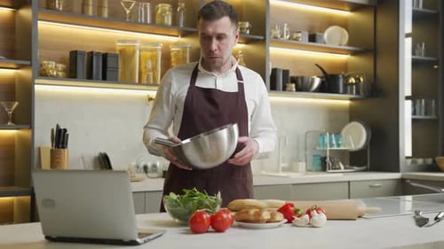 Man Prepares Meal in Kitchen with Laptop