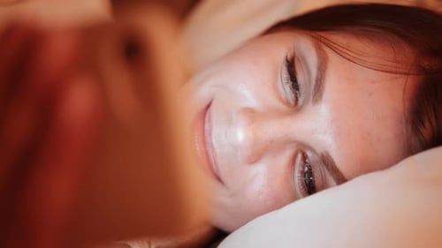 Smiling Woman Looks at Her Phone in Bed