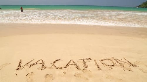 VACATION written in the beach sand washed aways by waves.