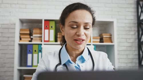 Mature Woman Doctor is Sitting at Cabinet of Modern Hospital Consulting Her Patient By Laptop