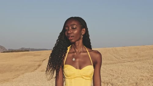 Linda mulher em vestido amarelo brilhante andando em campos abertos de braços abertos