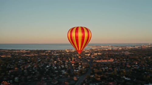 Yellow and Orange Striped Hot Air Balloon Floating Above City Streets
