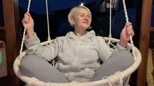 La jeune fille se balance sur une balançoire le soir et sourit