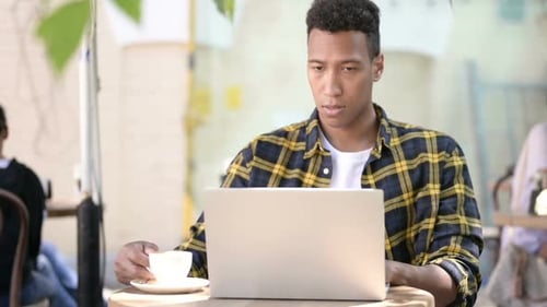 Young African Man Drinking Coffee and Working on Laptop Outdoor Cafe