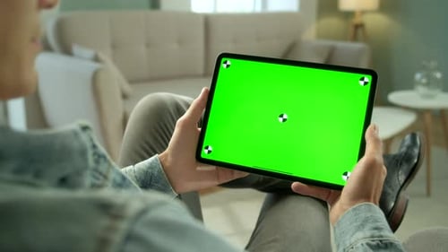 View From the Shoulder of Man Using Hand Gestures on Green Mock-up Screen Digital Tablet Computer in