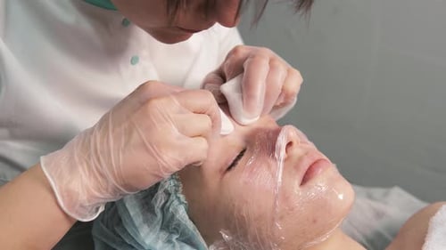 Cosmetologist Cleaning Woman's Face in Clinic
