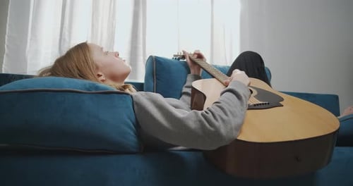 Side View of a Young Girl with Blond Hair Lies on a Sofa in a White Living Room