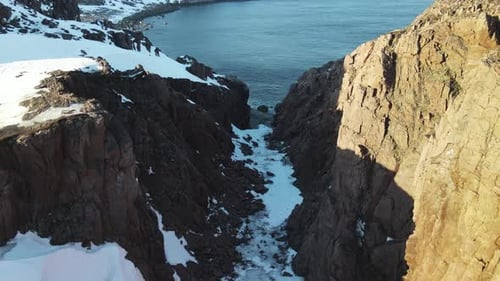 Winter Aerial Flight Through Scenic Canyon Top Over Waves Rolling on Artic Ocean Shore with Round