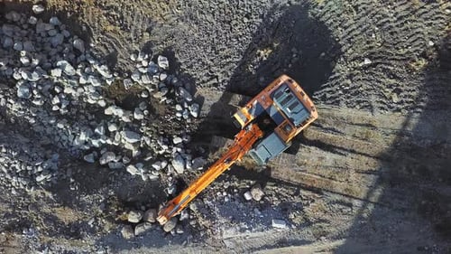 Large yellow excavator or bulldozer takes stones with bucket and fills hole.