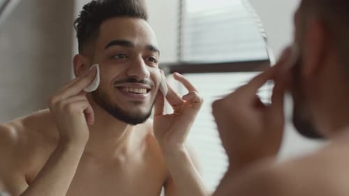 Young Adult Man Cleans Face in Bathroom Mirror