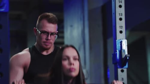 Woman Doing Barbell Squats with Trainer in Gym