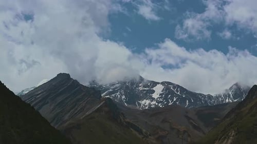 Timelapse Clouds Swirl Over a Mountain Valley a Snowy Peak in the Distance