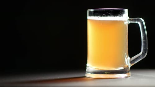 Caneca grande cheia de bebidas refrescantes de cerveja dourada, rotação lenta, isolada no fundo preto do estúdio