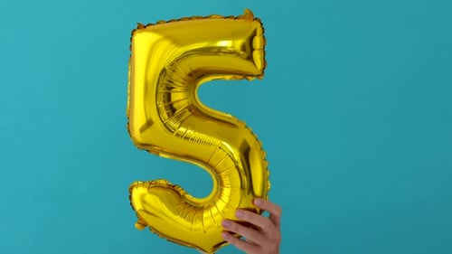 Gold Number Five Balloon Held Against Blue Background