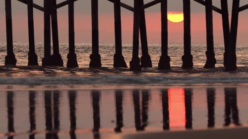 Sun setting behind pier reflecting on beach