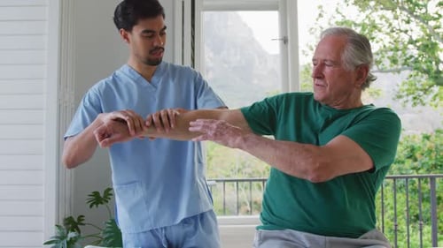 Slow motion of biracial male physiotherapist examining retired senior man's arm at nursing home