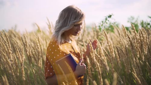 Beautiful Happy Young Woman in Field of Spikelets and Wheat with Book on the Sunset Blonde in the
