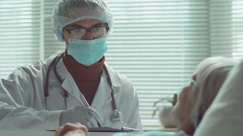 Doctor Writing Notes about Patient in Hospital Bed
