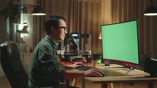 Asian Man Work On 3D Printer And Personal Computer With Mock Up Green Screen Display In Home Office