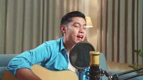 Hombre asiático tocando la guitarra y cantando una canción mientras transmite en vivo para su canal de redes sociales