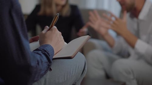 Un psychologue prend des notes dans un carnet, une paire de membres de la famille jure