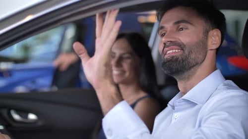 Excited Young Couple Sitting in Car at Dealership