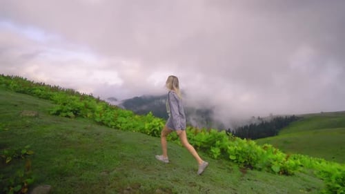 Woman Walking on Grassy Hillside on Cloudy Day