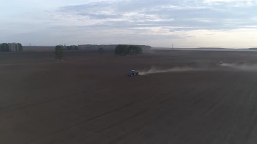 Two tractors plow in a huge field, Spring, evening 01
