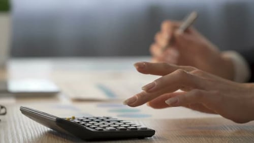 Hands Calculating Finances and Writing on Charts