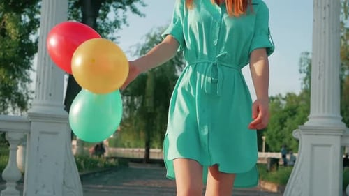 Young Woman Walks with Balloons in a Park