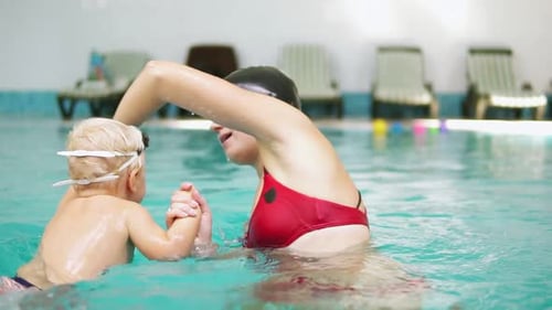 Zeitlupenaufnahme eines glücklich lächelnden kleinen Kindes, das zusammen mit seiner Mutter im Schwimmbad schwimmt