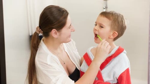 Woman Helping Child Brush Teeth in Bathroom