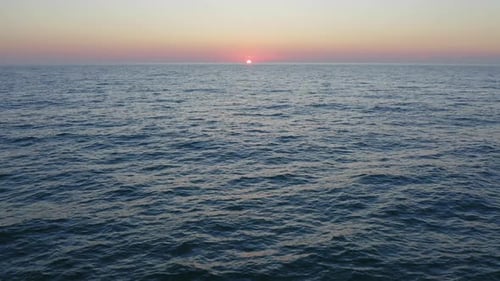 Vuelo aéreo sobre la superficie del agua del mar con olas tranquilas al atardecer, cielo naranja brillante