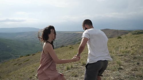 The Happy Couple Holding Hands Running Along a Plain Under the Overcast Sky