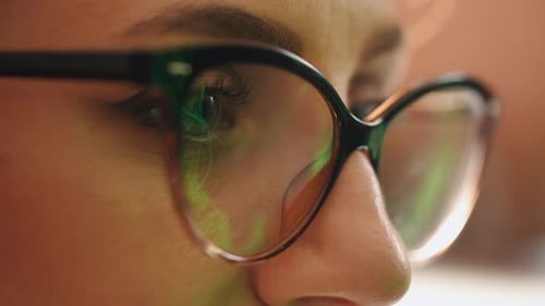Businesswoman working at night, reflections in eyeglasses.