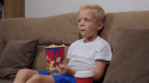 Child Sits on Couch Watching Something with Popcorn