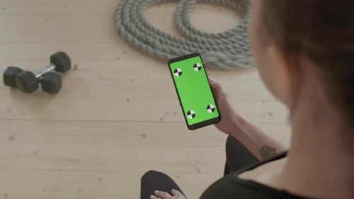 Woman Holding Smartphone with Green Screen in Gym