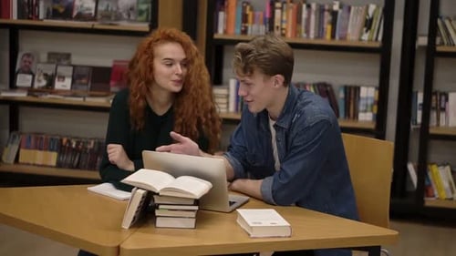 Young Male and Female Students Talking Using Laptop Explaining Course Work Study Together in Library