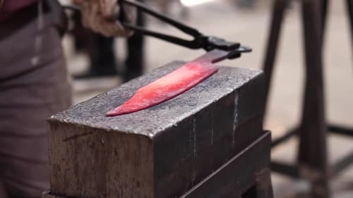 Blacksmiths forging hot metal with hammer in workshop
