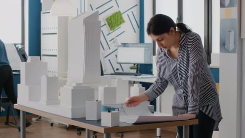 Woman Architect Analyzing Blueprints Plan on Table to Design Building Model and Maquette