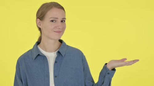 Young Woman Presenting with Hand Gesture on Yellow