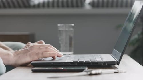 An Unrecognizable Man Uses Mobile Internet From His Smartphone to Work on a Laptop