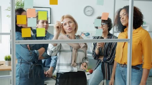 Creative Business Team Writing on Board with Sticky Notes Discussing Ideas Working in Office