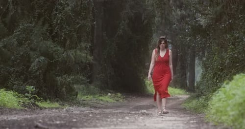 Young beautiful woman with a red dress walking in a green forest