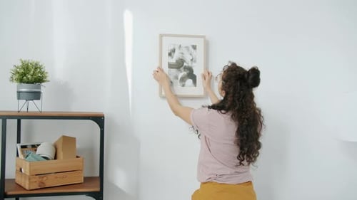 Young Woman Hanging Picture on Wall Decorating House Improving Interior