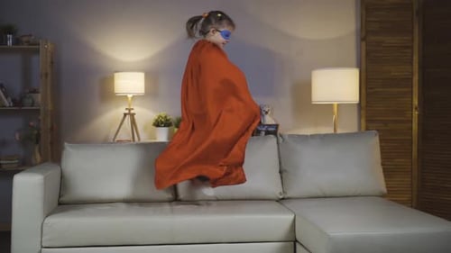 Girl Jumps on Couch Wearing Red Cape Indoors
