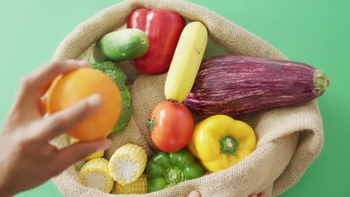 Vídeo de mujer birracial arreglando frutas y verduras frescas en bolsa rústica sobre fondo verde