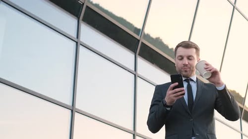 Man in Suit Drinks Coffee, Uses Smartphone